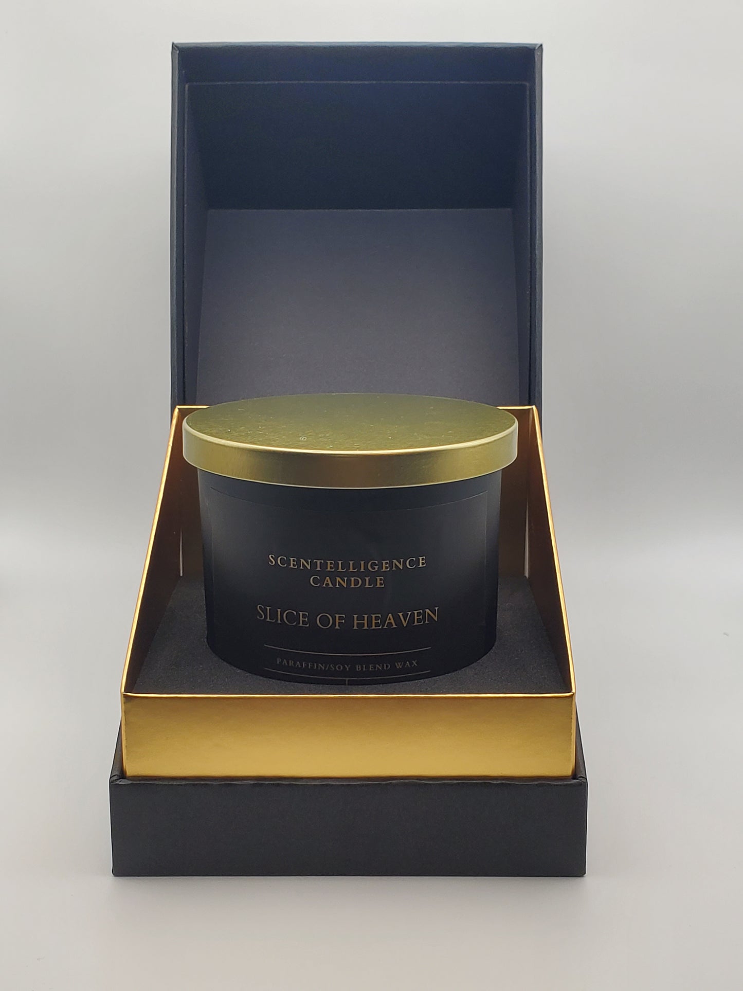 Slice of Heaven candle nestled inside signature black and gold gift packaging, styled against a grey background for a refined, gift-ready presentation.